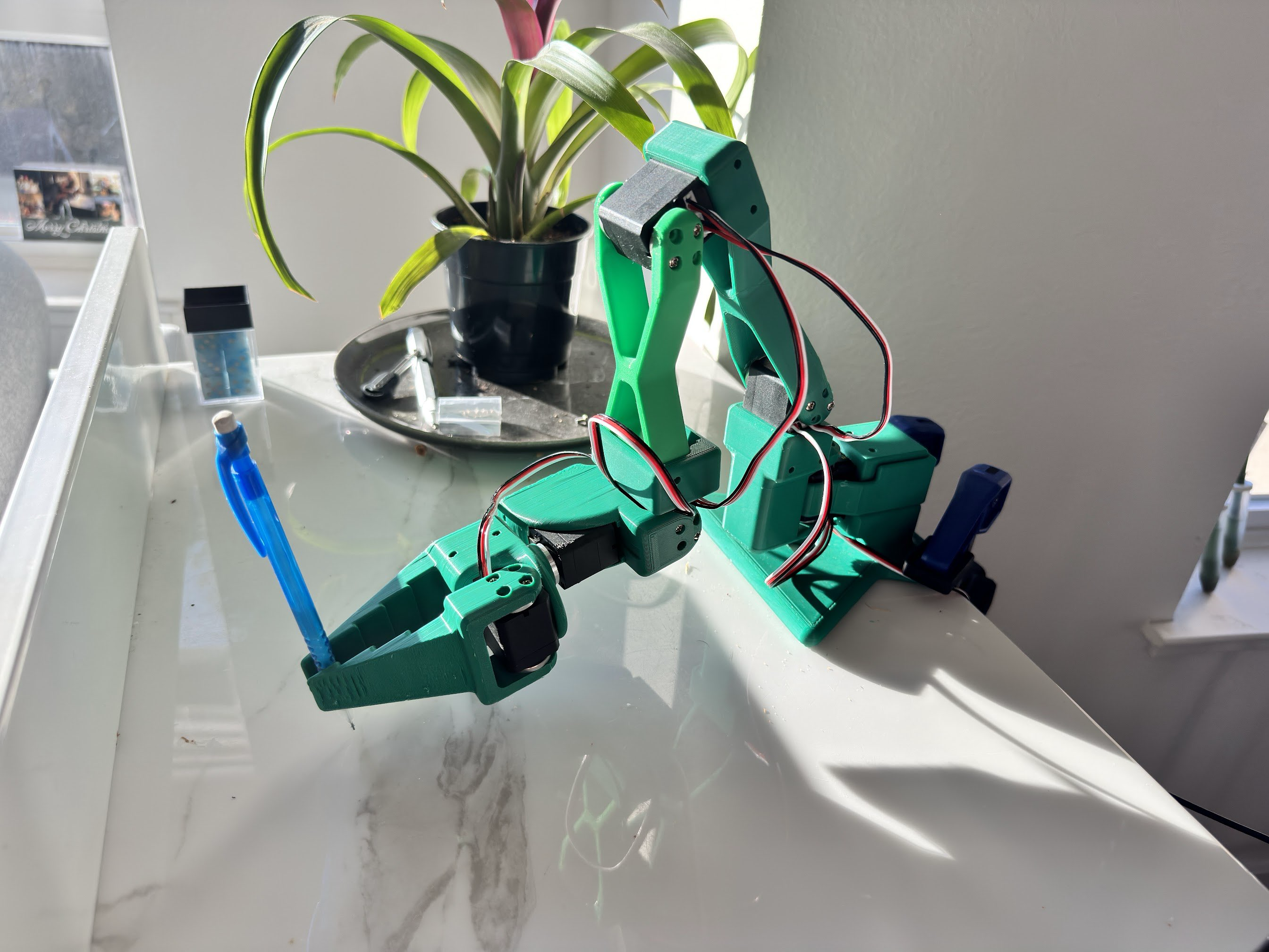 Fully assembled 6-DOF robot arm holding a pen, demonstrating precision control and end-effector positioning accuracy.